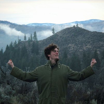 Corey Boiko with arms raised on a misty mountain ridge